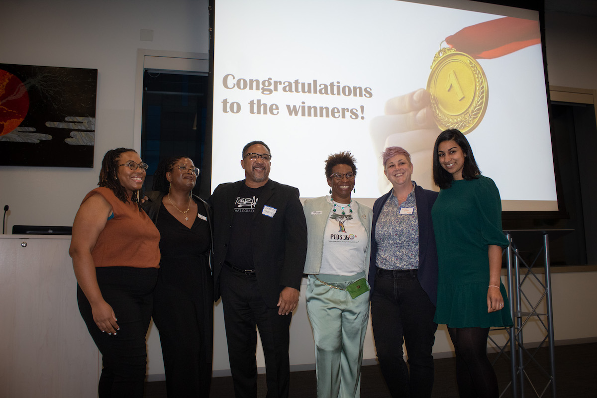 Group of people posing for a photo at an event with a screen in the background reading "congratulations to the winners!.