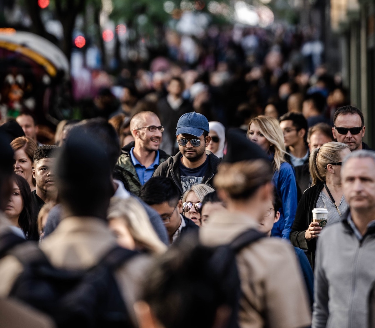 A crowded urban street with pedestrians of diverse appearances moving in various directions.