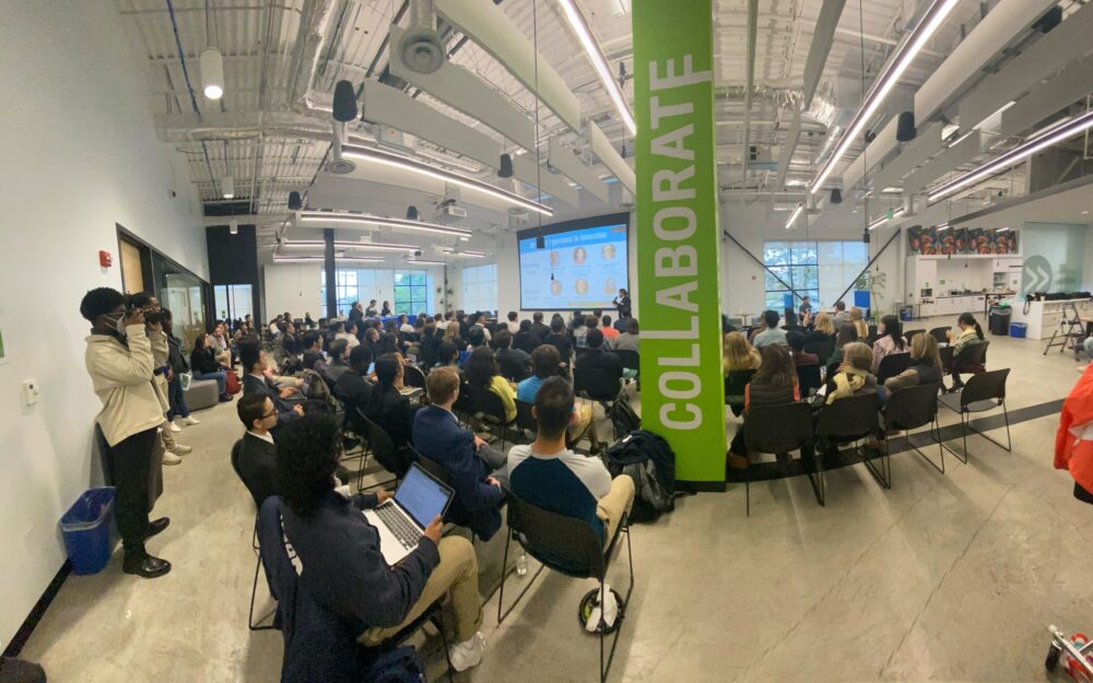 Audience attending a presentation in a modern conference room with a "collaborate" banner on display.