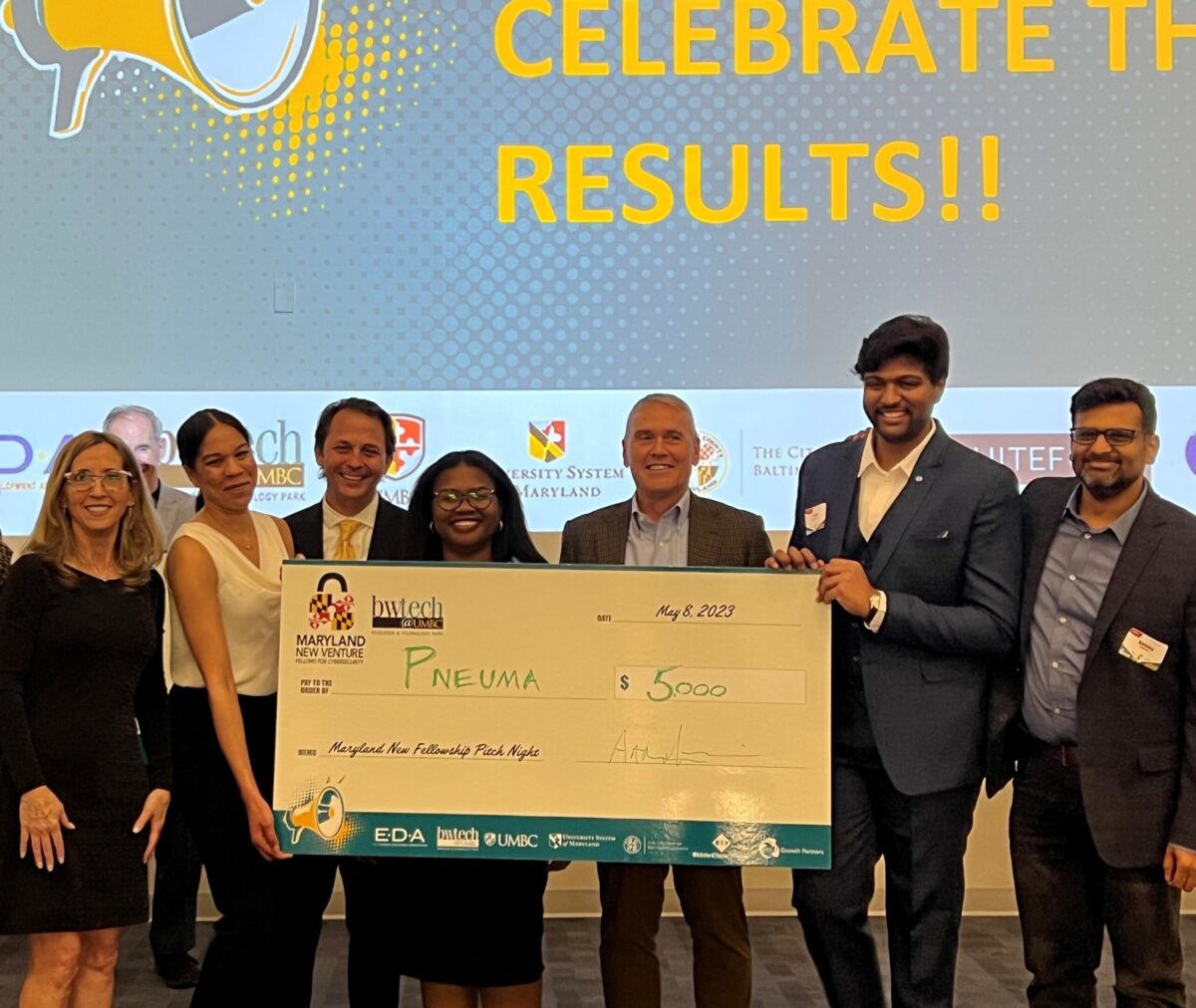Group of people holding an oversized check for $5000 to pneuma at an award event.