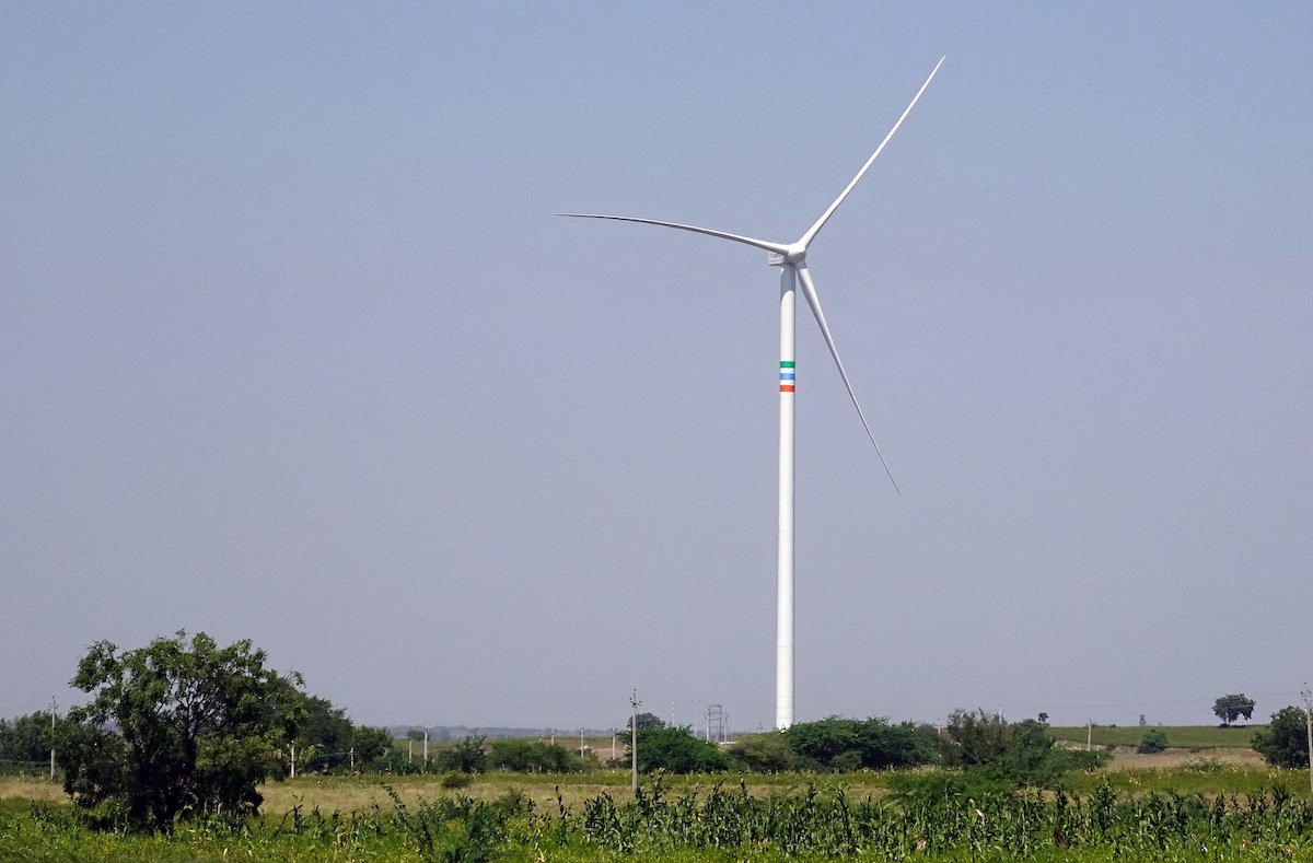 A solitary wind turbine stands in a green field under a clear sky.