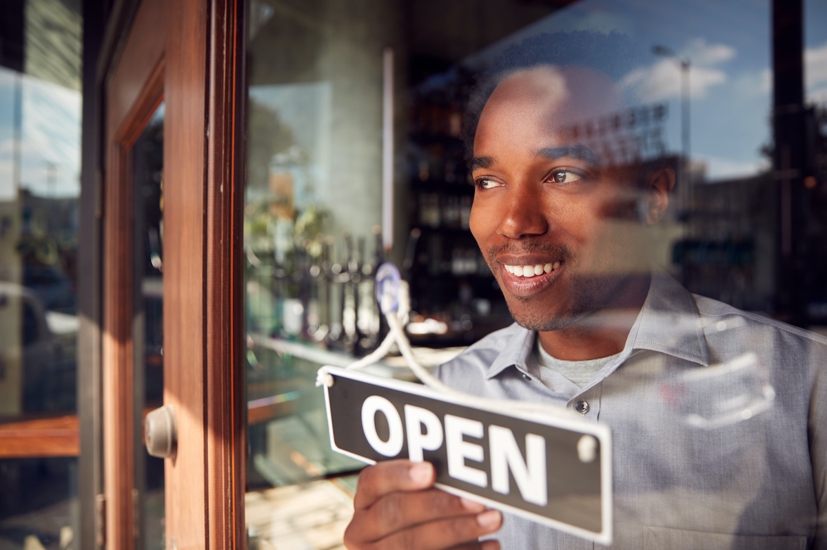 A Black store owner turns the "open" sign on his front door.
