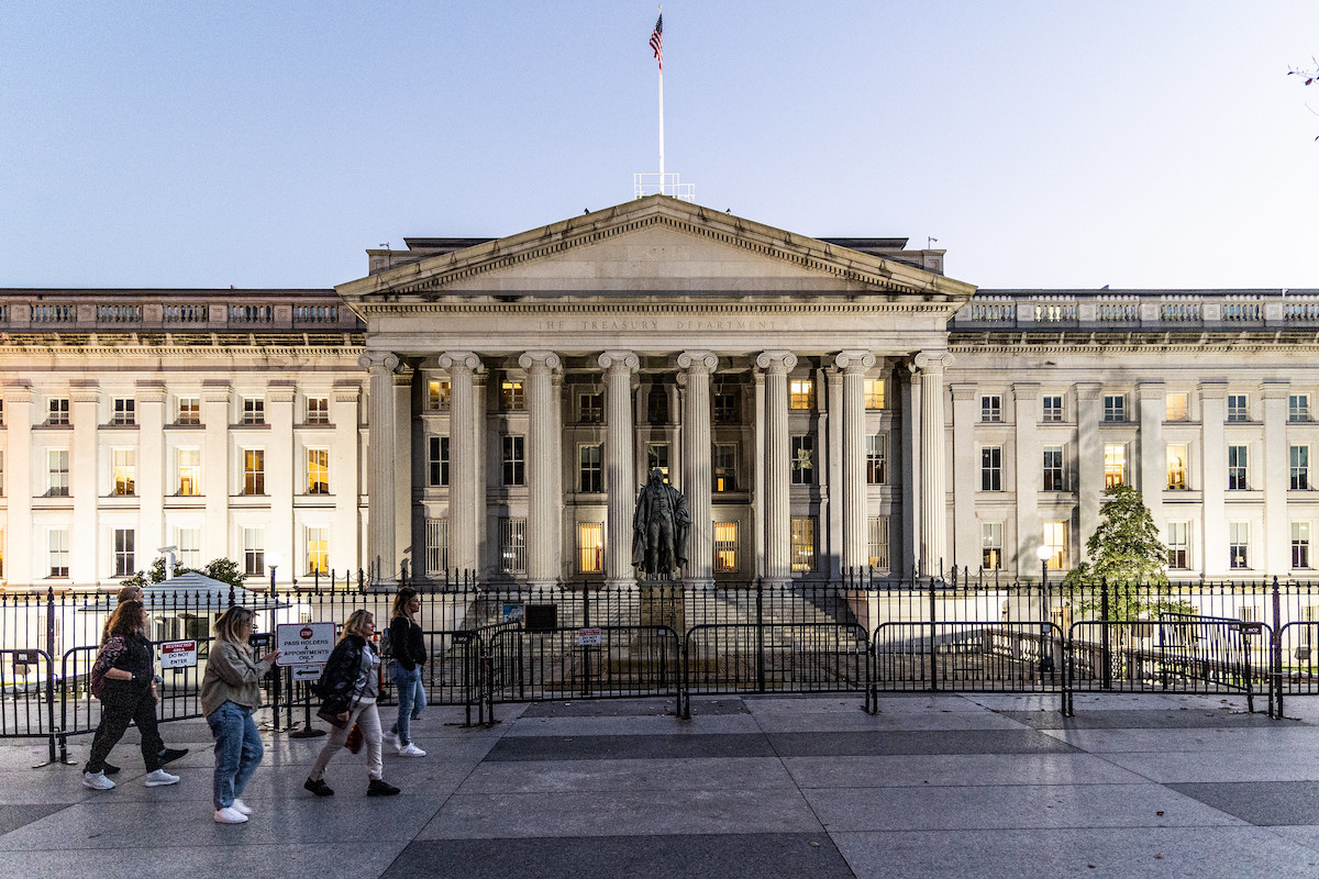 Treasury building in beige and white in front of white-blue sky on grey sidewalk