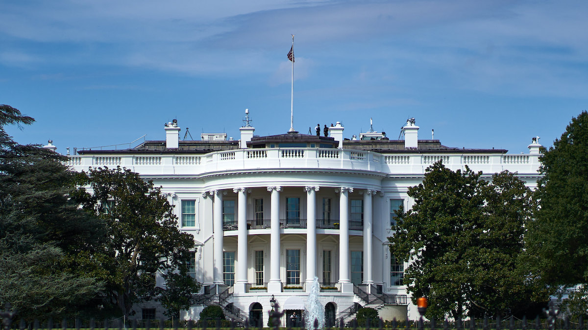 White House surrounded by green trees in front of blue and white sky
