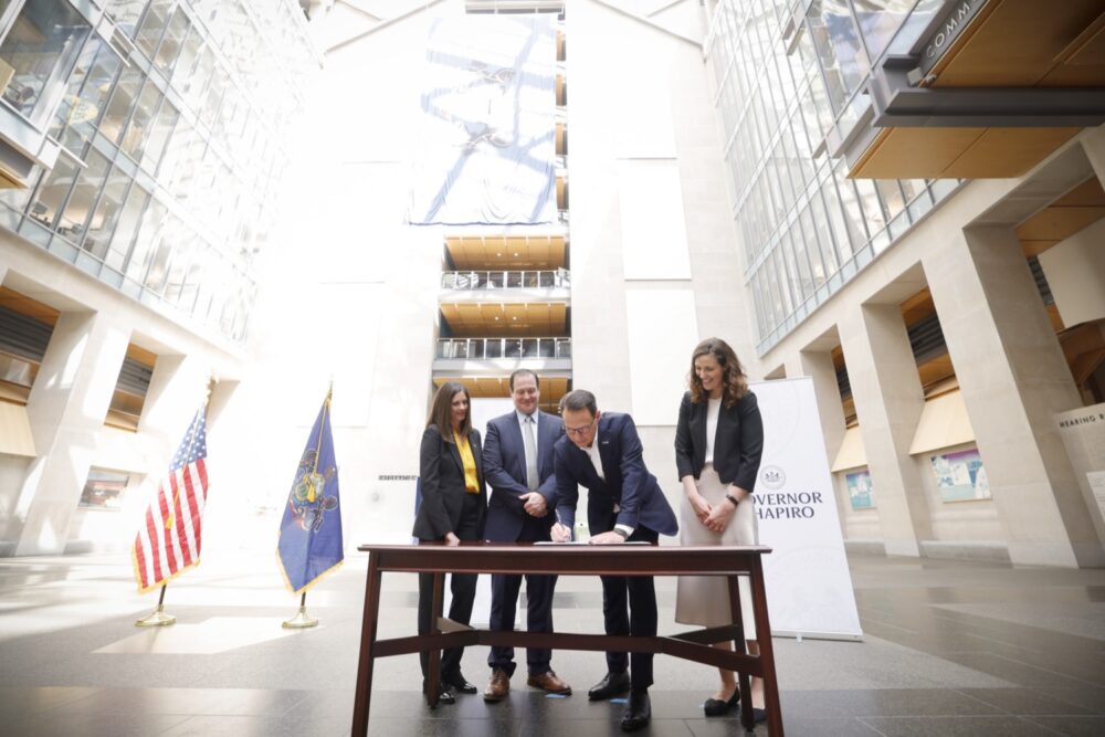 Three people standing at a table signing a document.