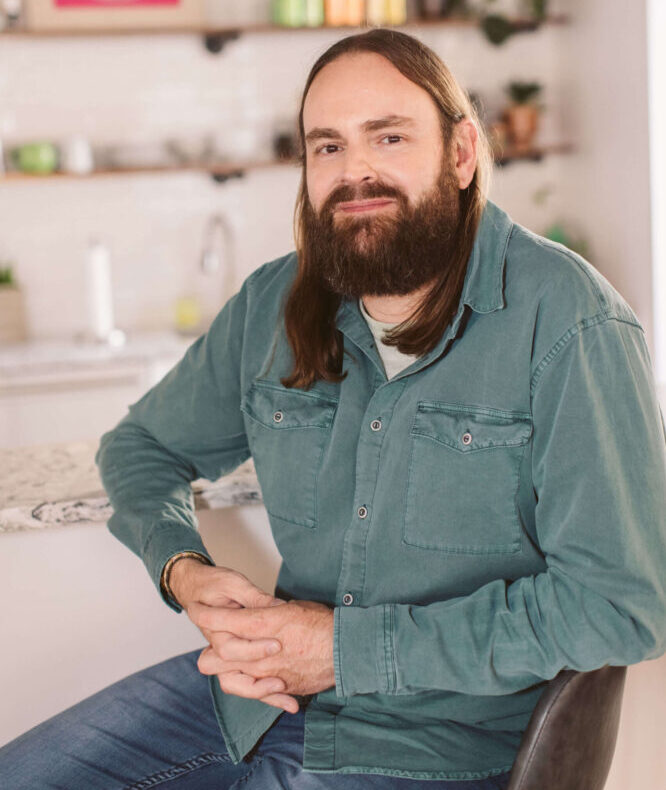 A bearded man sitting on a chair in a kitchen.