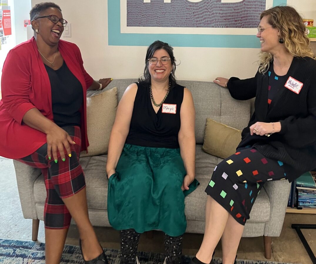 Three women sitting on a couch in front of a dhb sign.