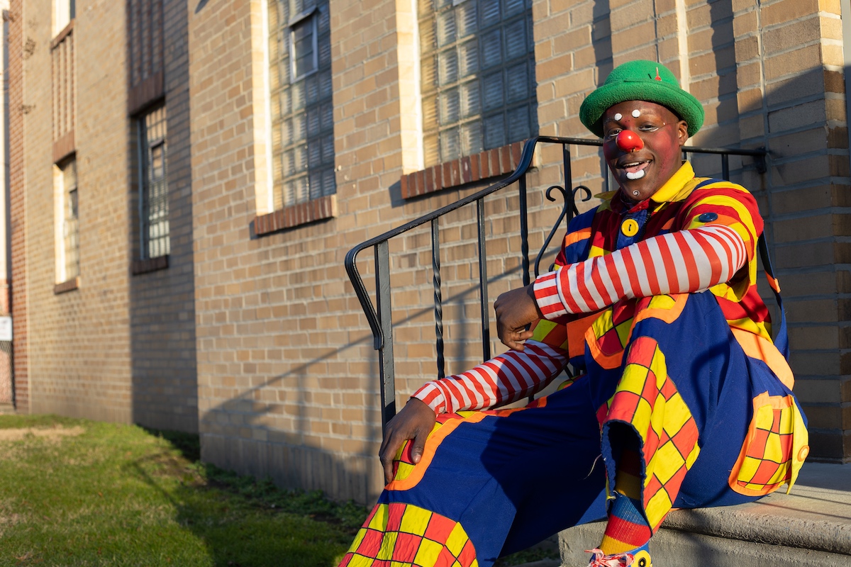 A clown sitting on the steps of a building.