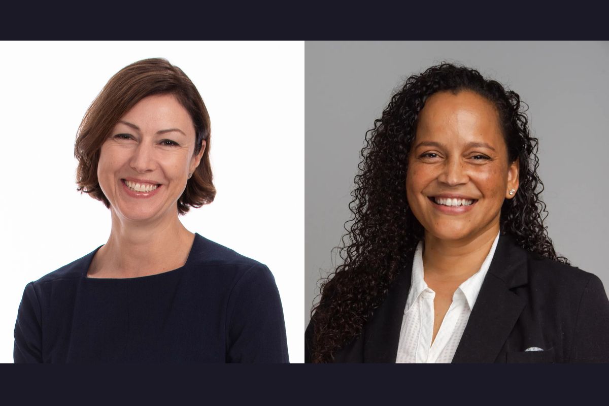 Two women smiling, one with short brown hair wearing a dark top on the left, and the other with long curly hair wearing a white shirt and dark blazer on the right.