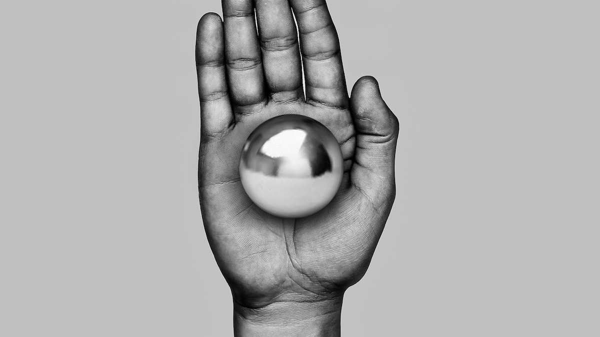 A grayscale image of an open hand holding a reflective metallic sphere.