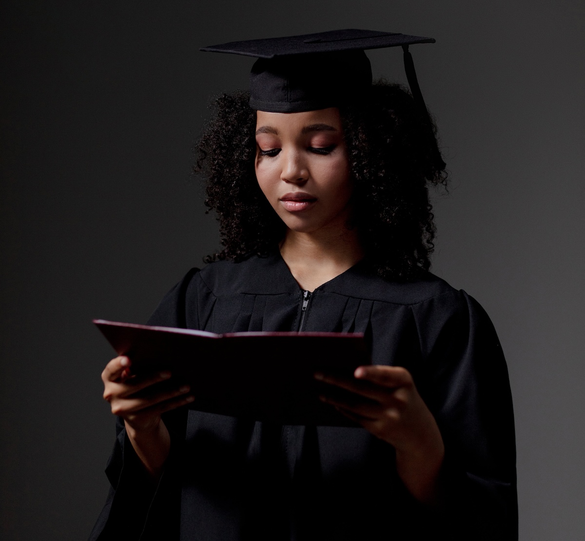 A woman in a graduation gown and cap looking down at her diploma.