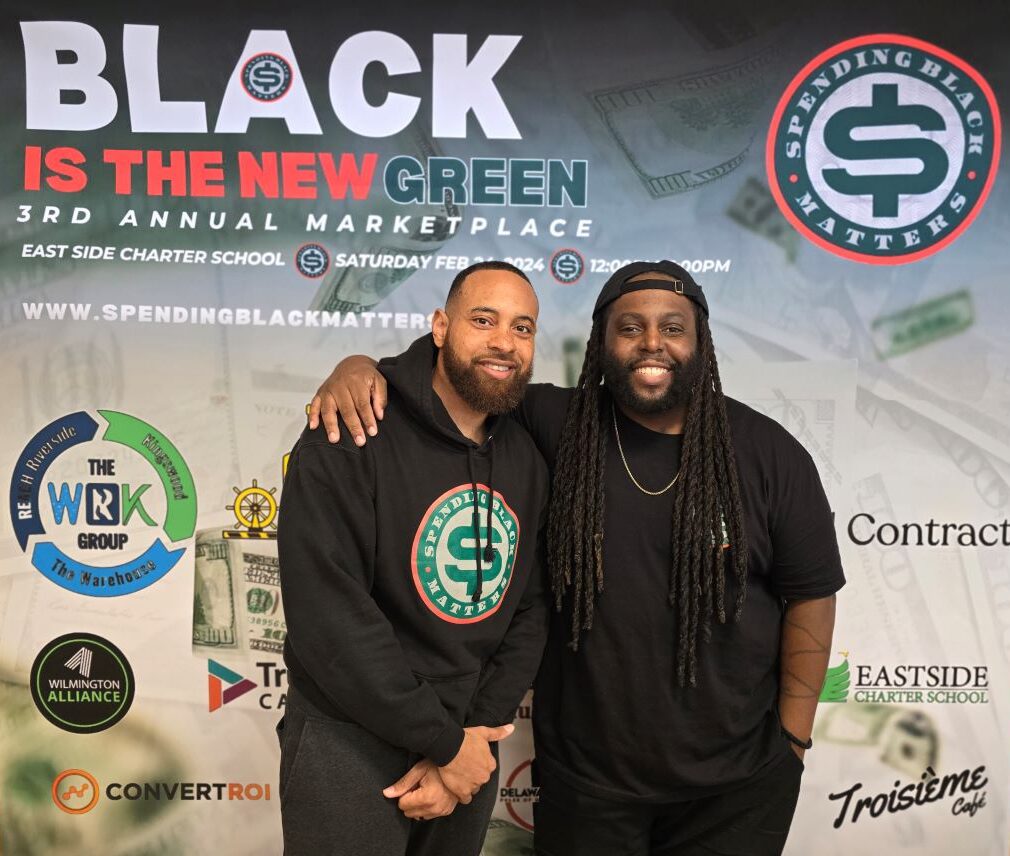 Two men standing in front of a banner that says black is the new green.