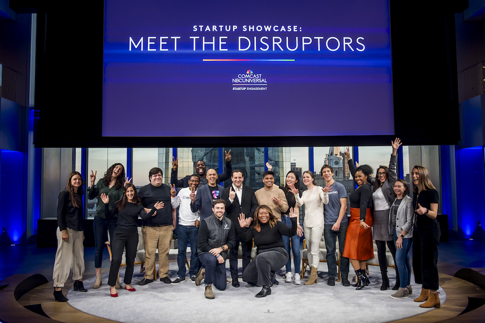 A group of people stand on a stage under a sign that reads "Startup Showcase: Meet the Disruptors"