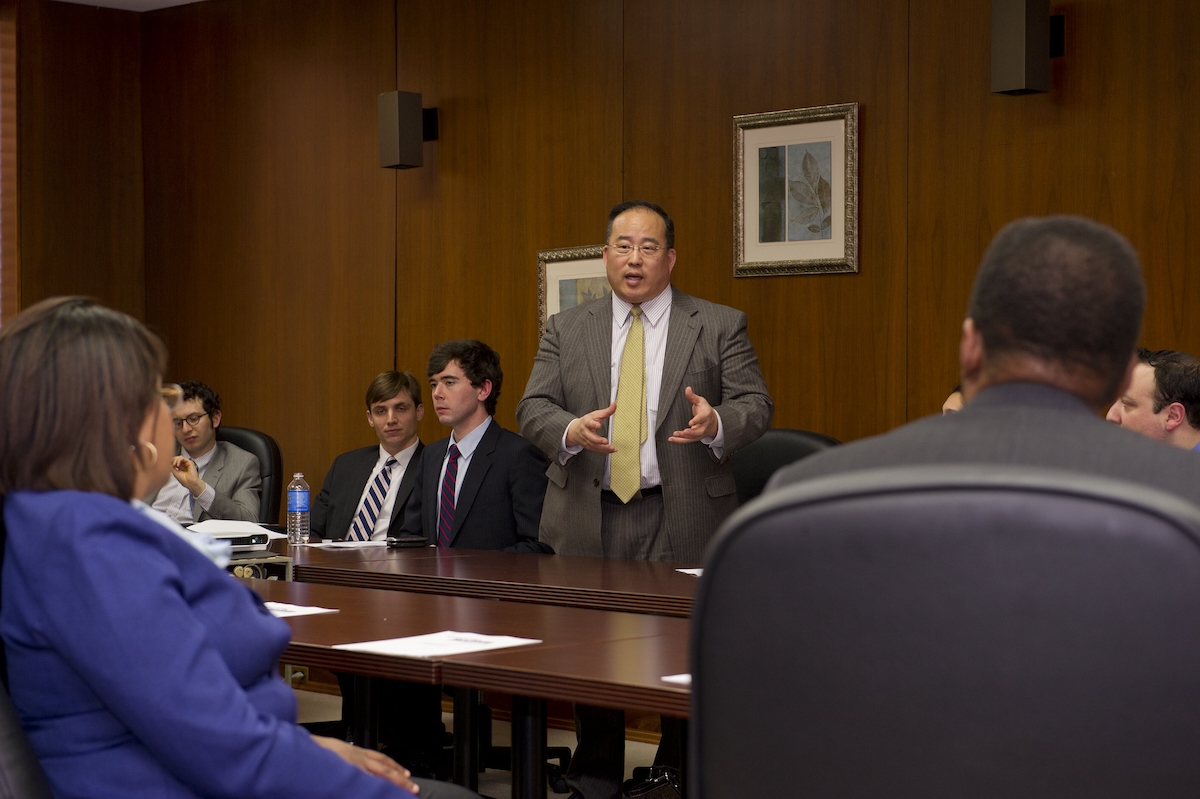 A man in a suit is speaking to a group of people in a conference room.