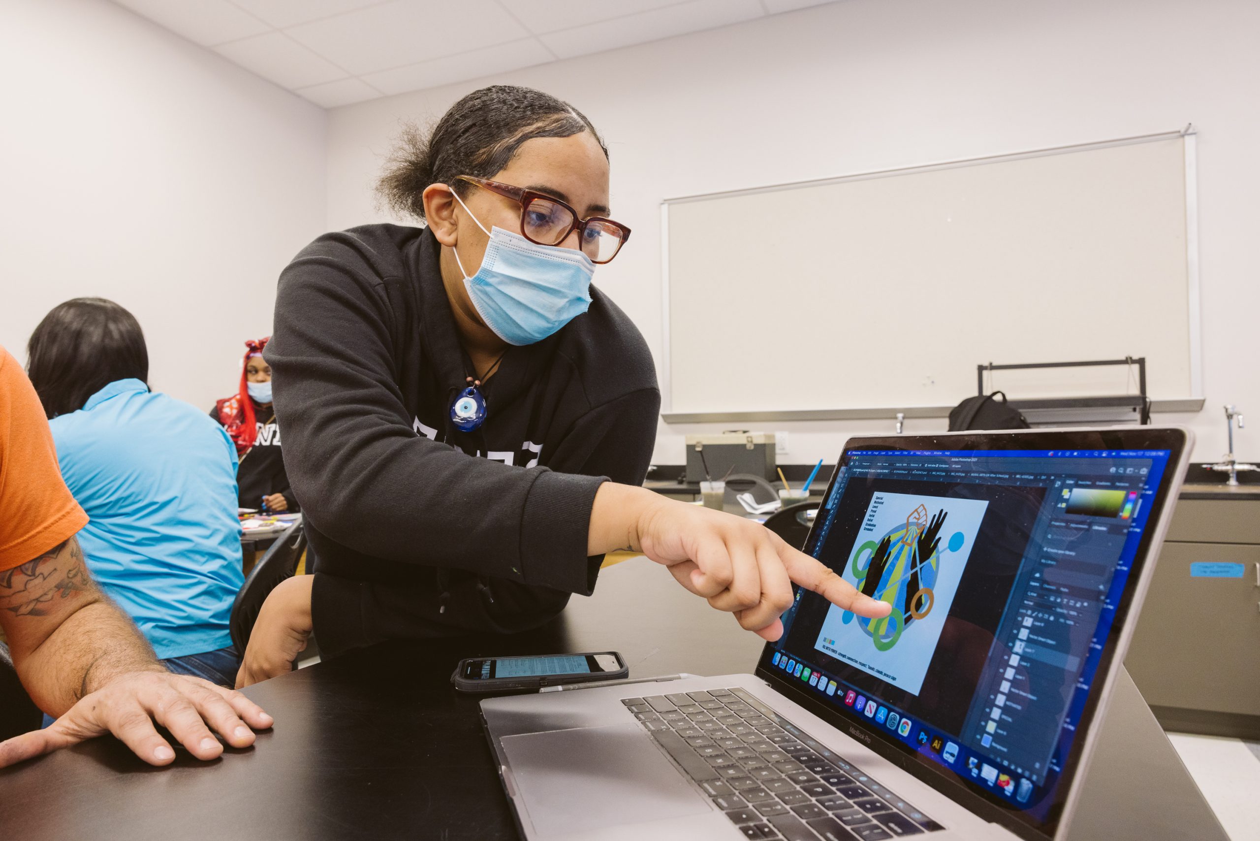 Woman in mask pointing at laptop for student