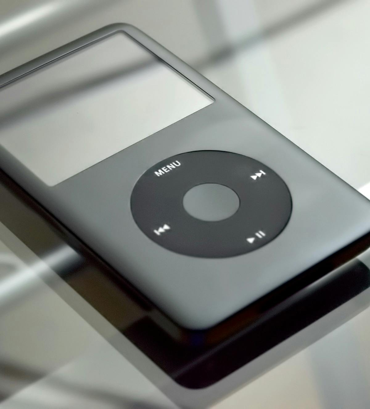 A black ipod sitting on a glass surface.