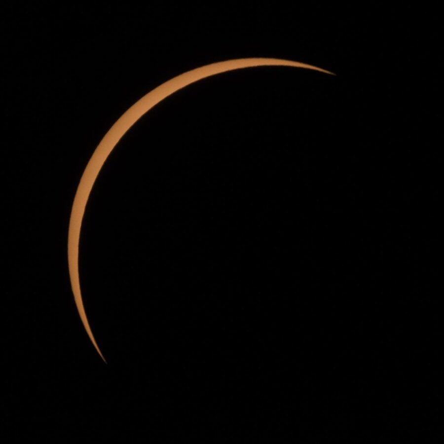 Black sky with orange sliver of sun during solar eclipse