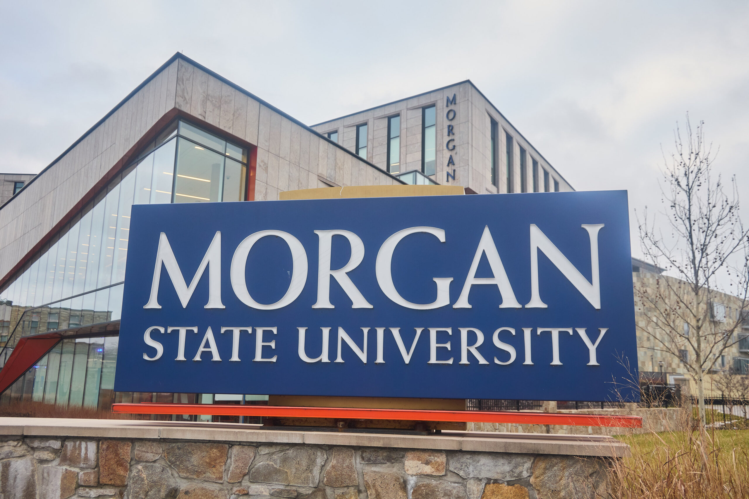 A large sign reads "Morgan State University" in front of a modern campus building with "Morgan" visible on the facade in the background.