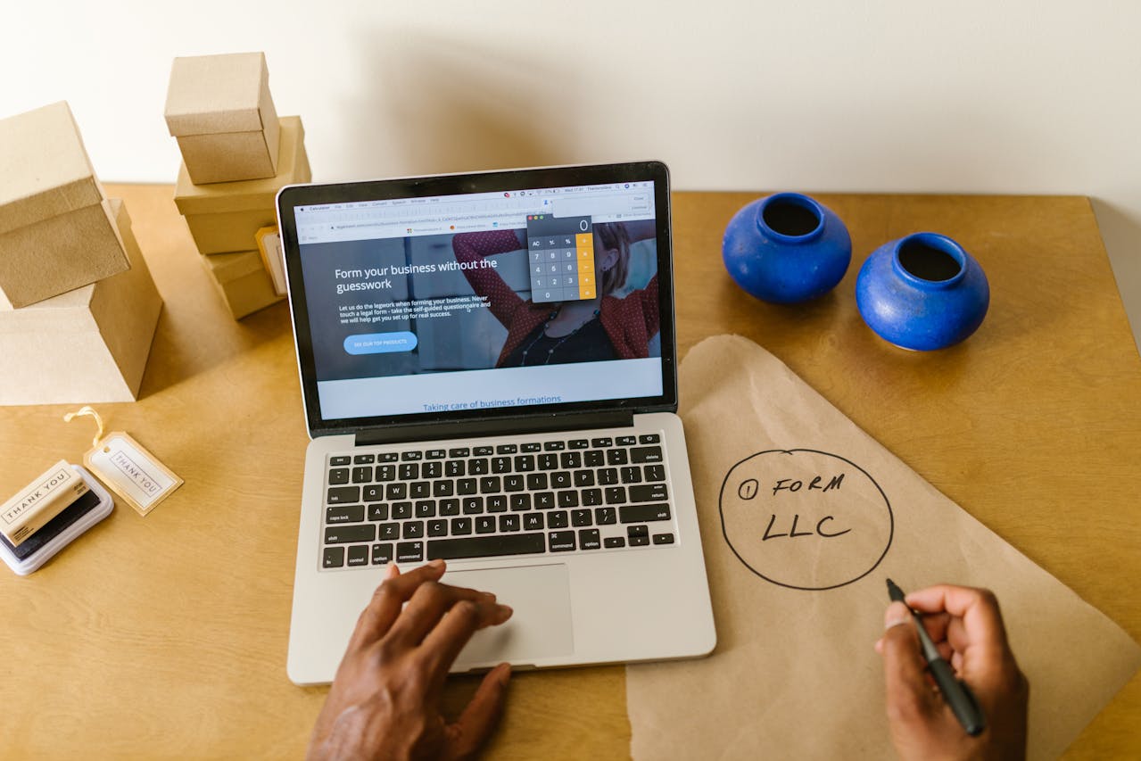 Person researching how to form an llc on a laptop with notepad and business supplies on a desk.