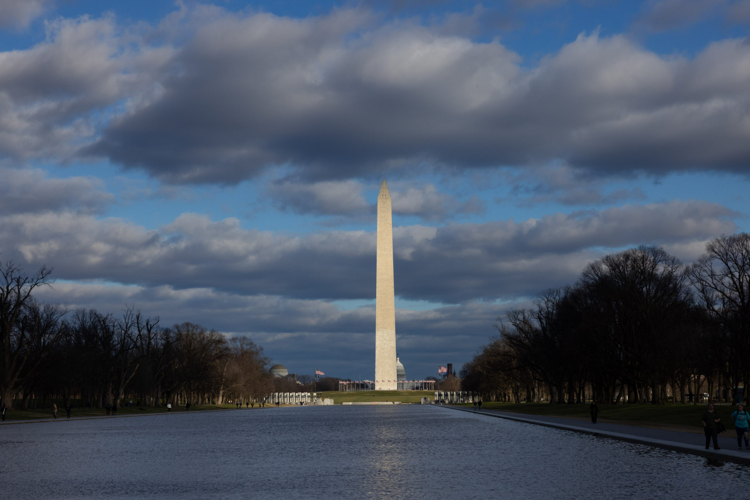 The washington monument standing tall under a cloudy sky, viewed across the reflecting pool in washington, d.c.
