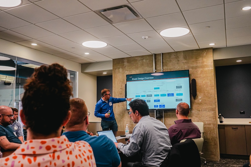 A presenter pointing at a digital screen during a corporate meeting in a conference room with attentive audience.