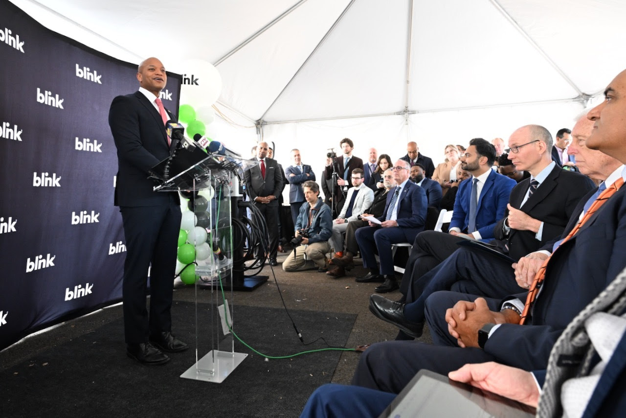 Gov. Wes Moore in suit at podium near audience of people in suits under white tent