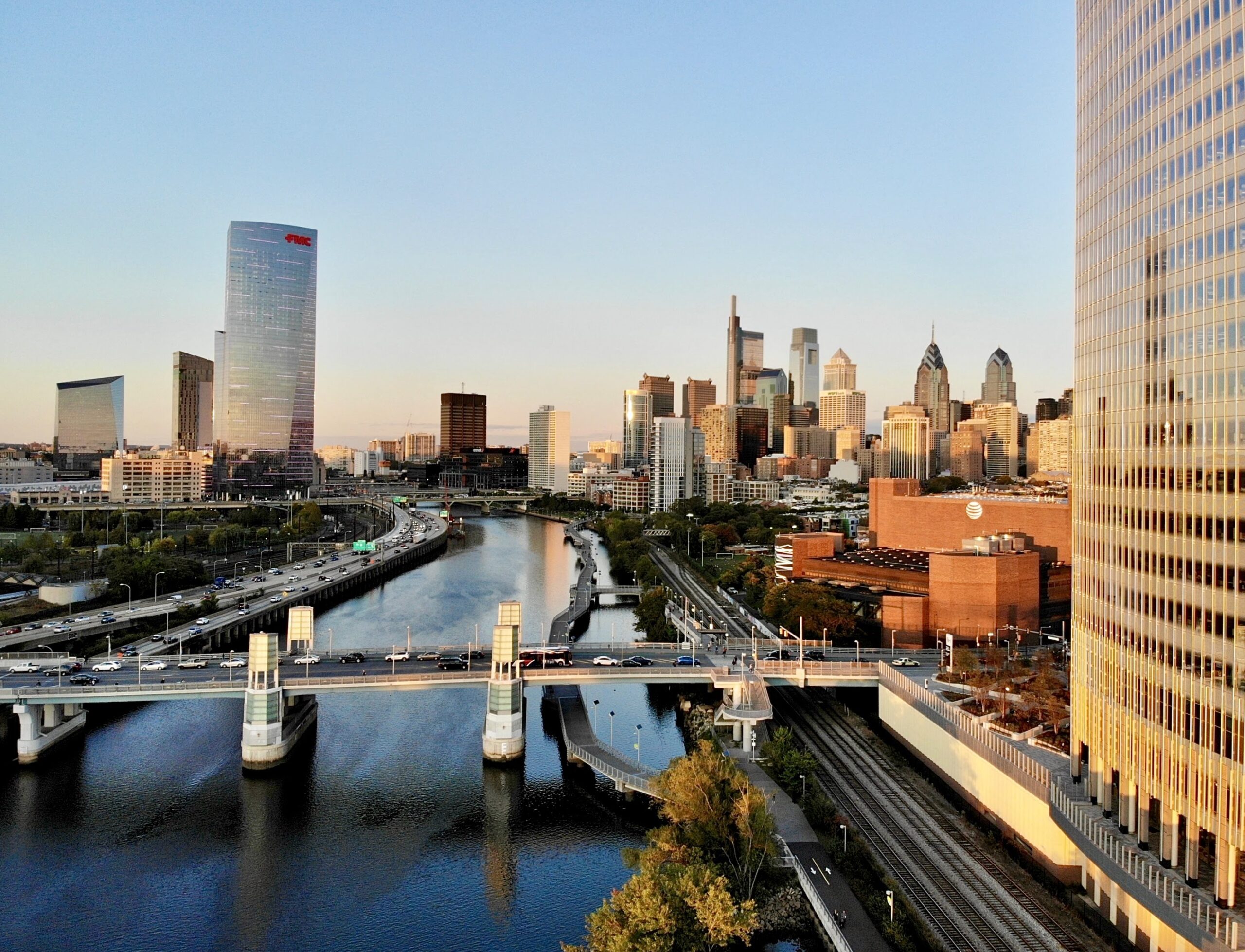 Aerial view of an urban skyline with skyscrapers, a riverfront, and a bridge at dusk.