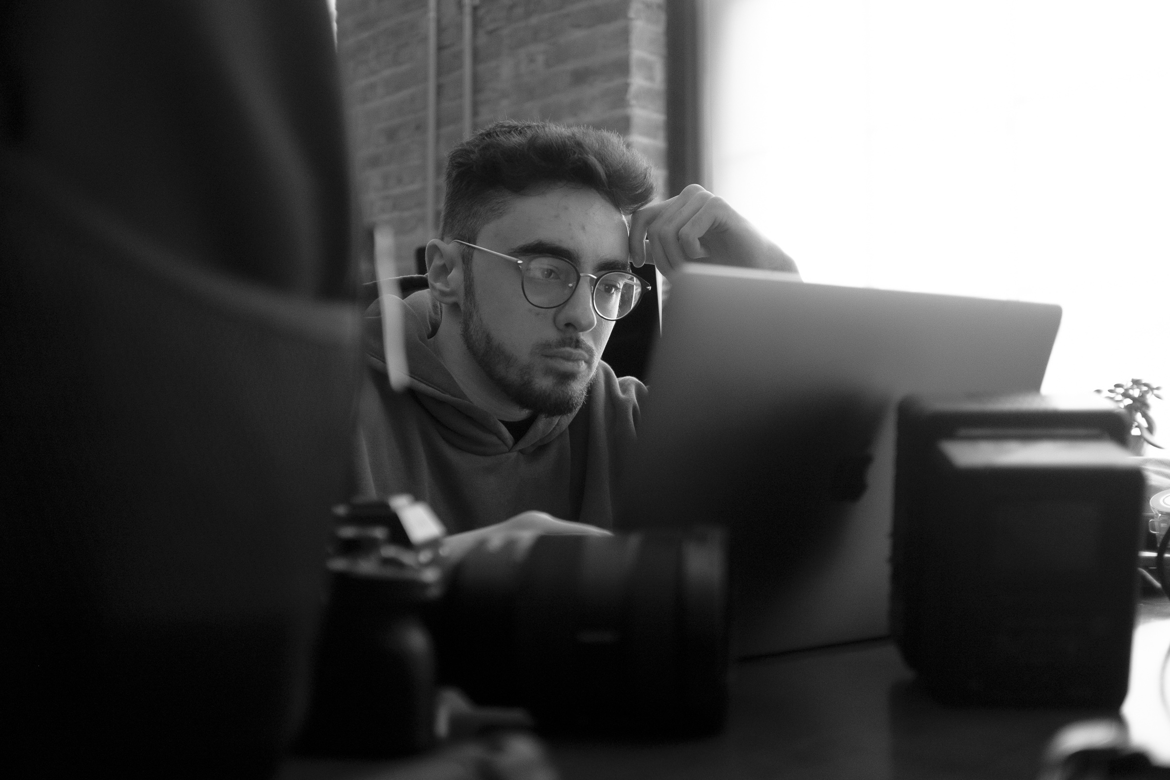 Black-and-white photo of man with beard and glasses at computer near camera