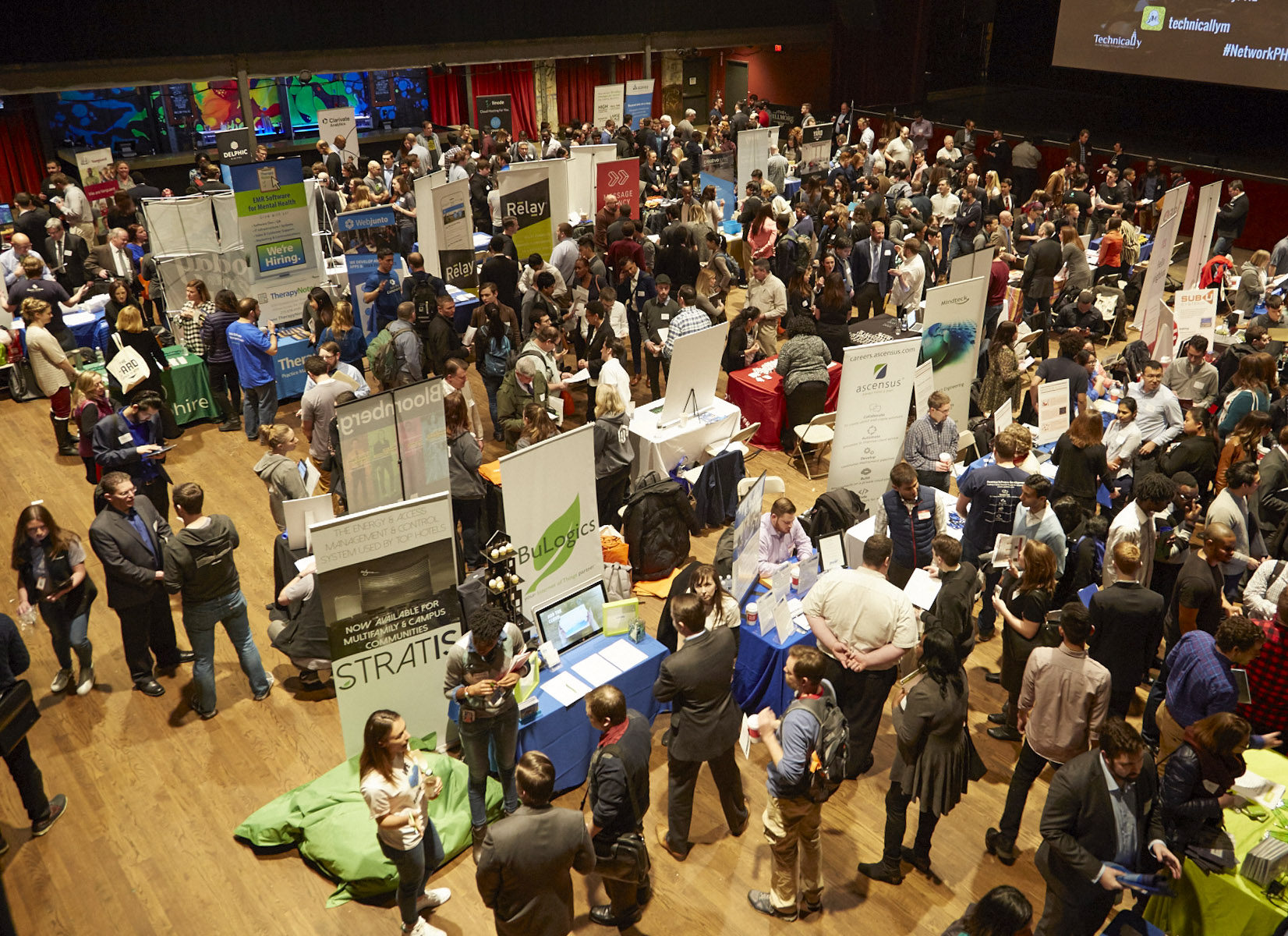 A large crowd attends an indoor career fair with multiple booths and banners, where people are networking and gathering information.