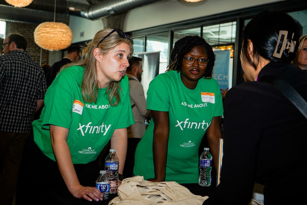 Two women in green Xfinity shirts talking with an jobseeker at a career fair.