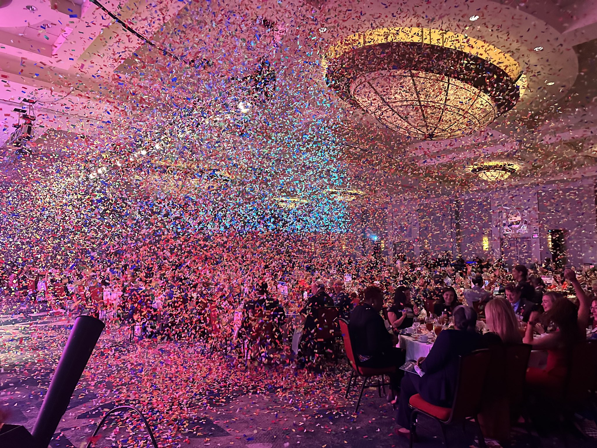 Confetti rains from the sky on a crowd bathed in pink light.