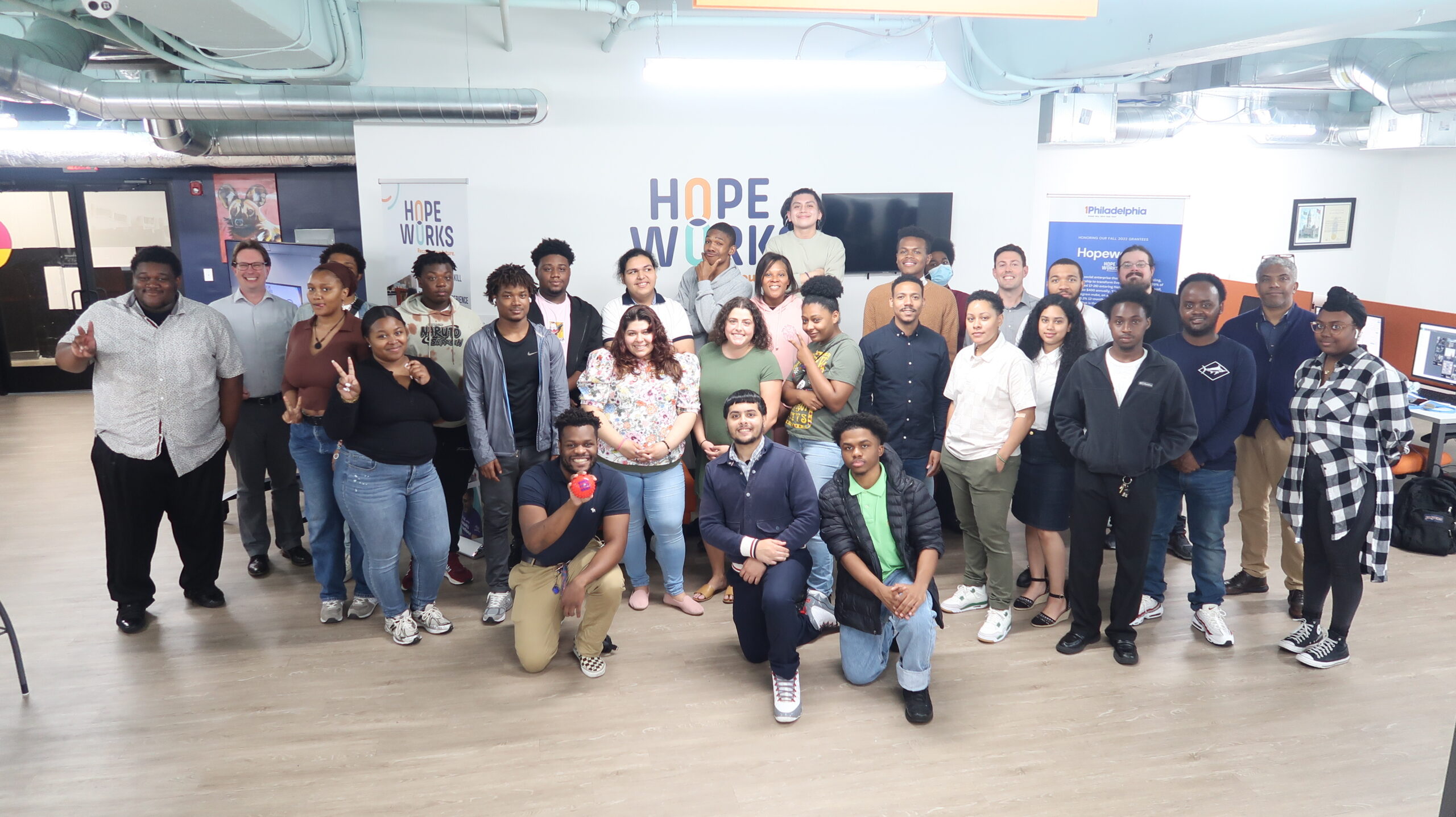 A diverse group of people posing and smiling in a room with "Hope Works" signage in the background.
