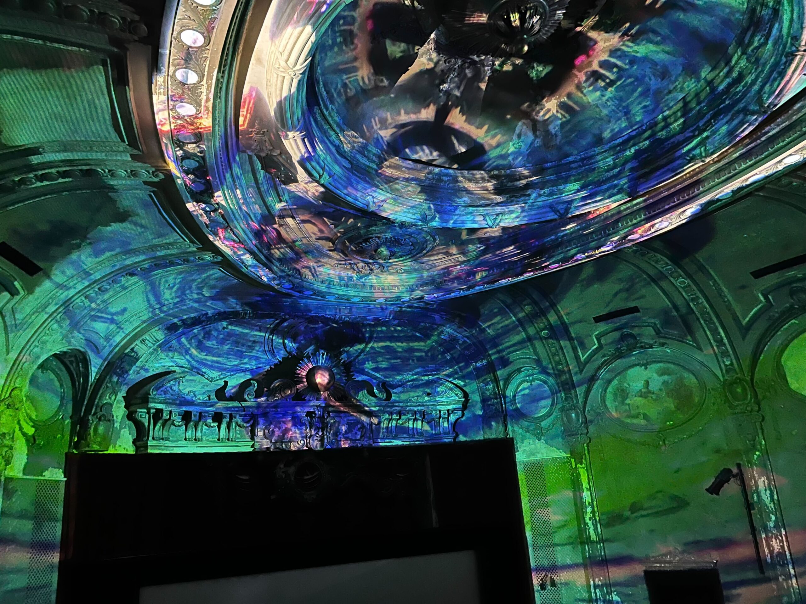 Green, blue and pink lights projected onto theatre walls.