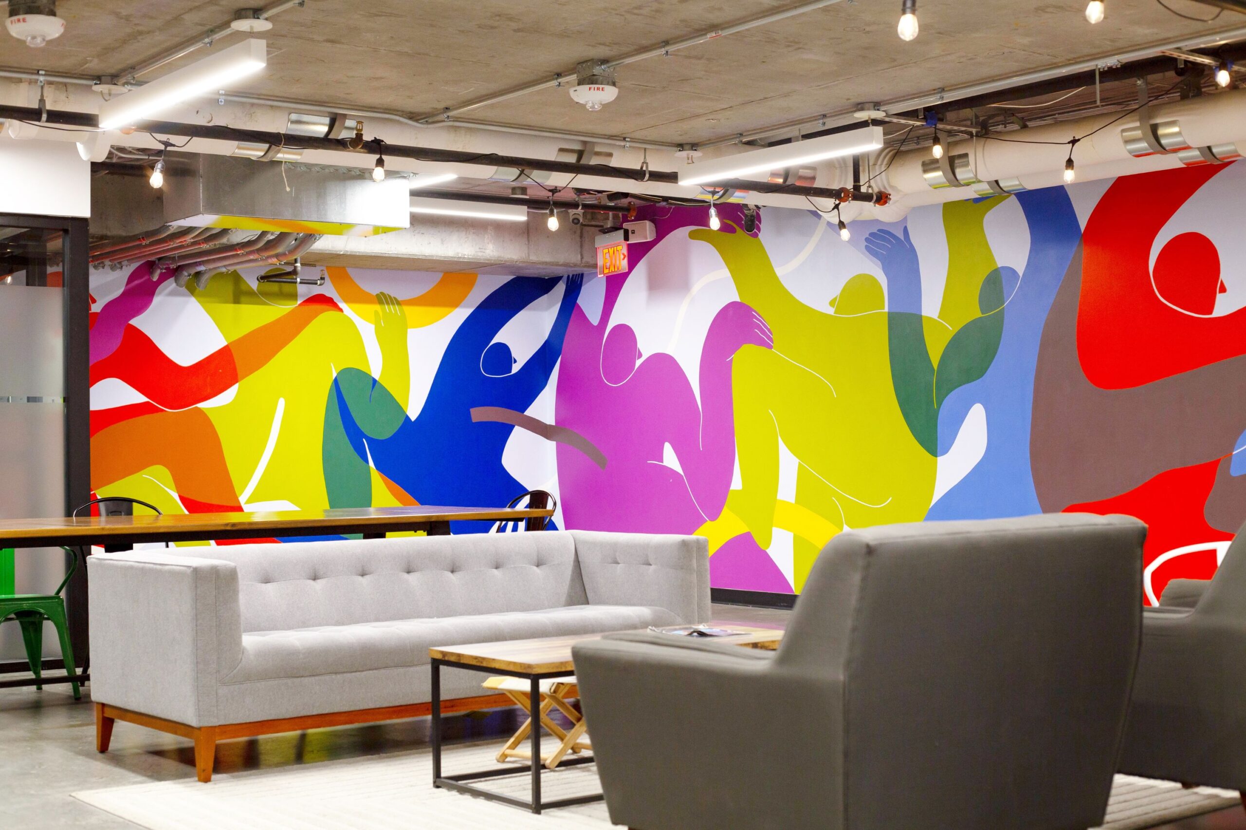 A colorful wall with couches, chairs and a table.