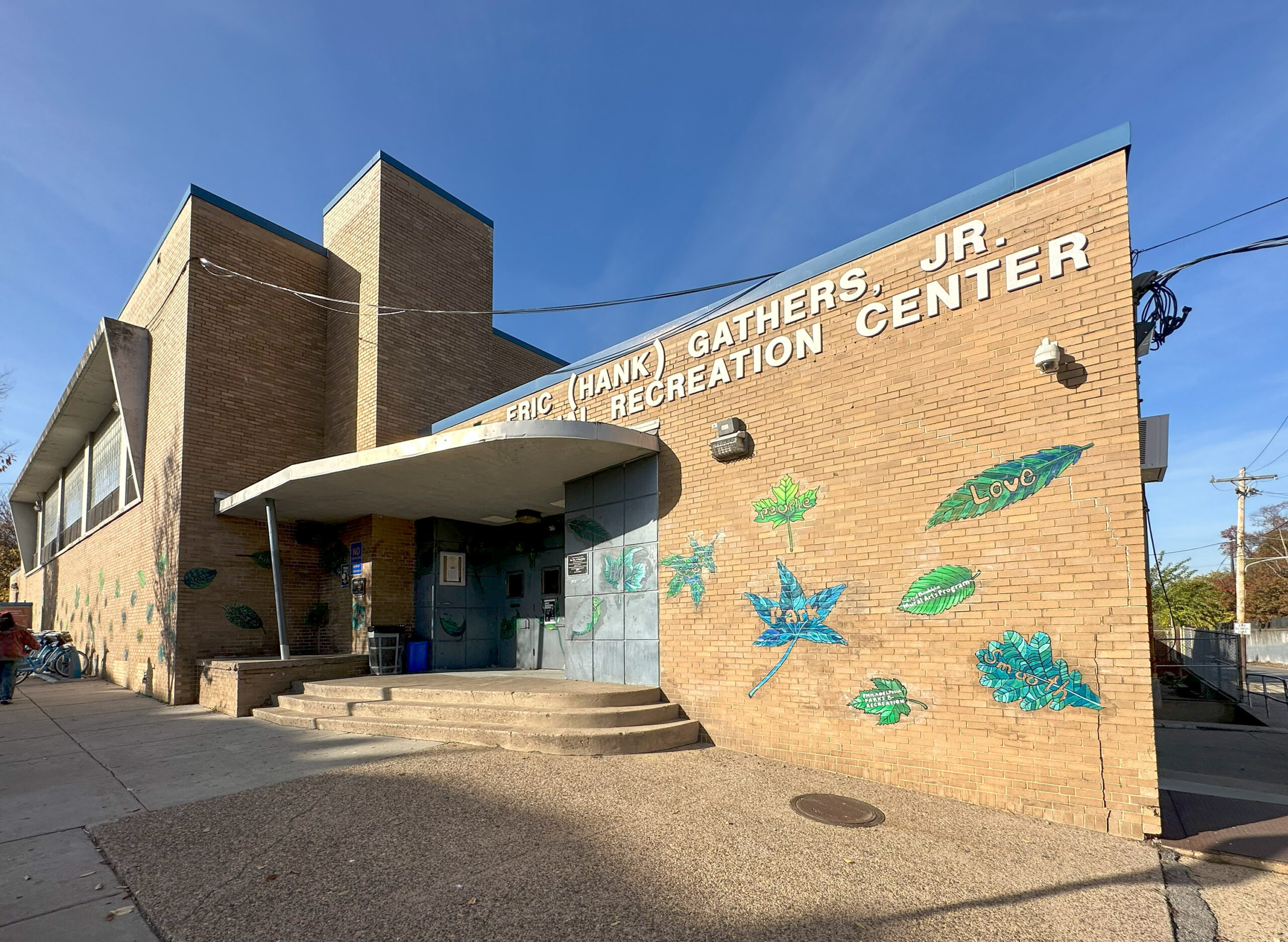 Brick building labeled with murals of plants and words "Peace" and "Love" on the wall. Steps and entrance are visible, with a clear sky above.