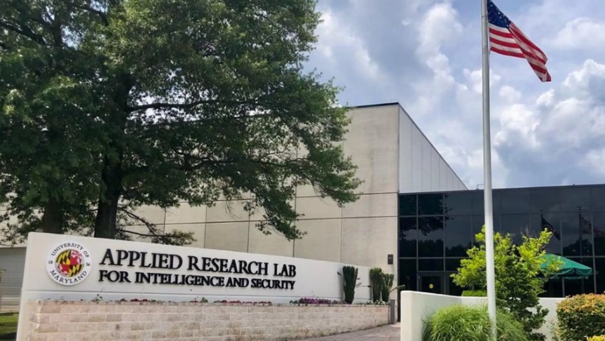Entrance of the Applied Research Lab for Intelligence and Security at the University of Maryland, with an American flag and a modern building in the background.
