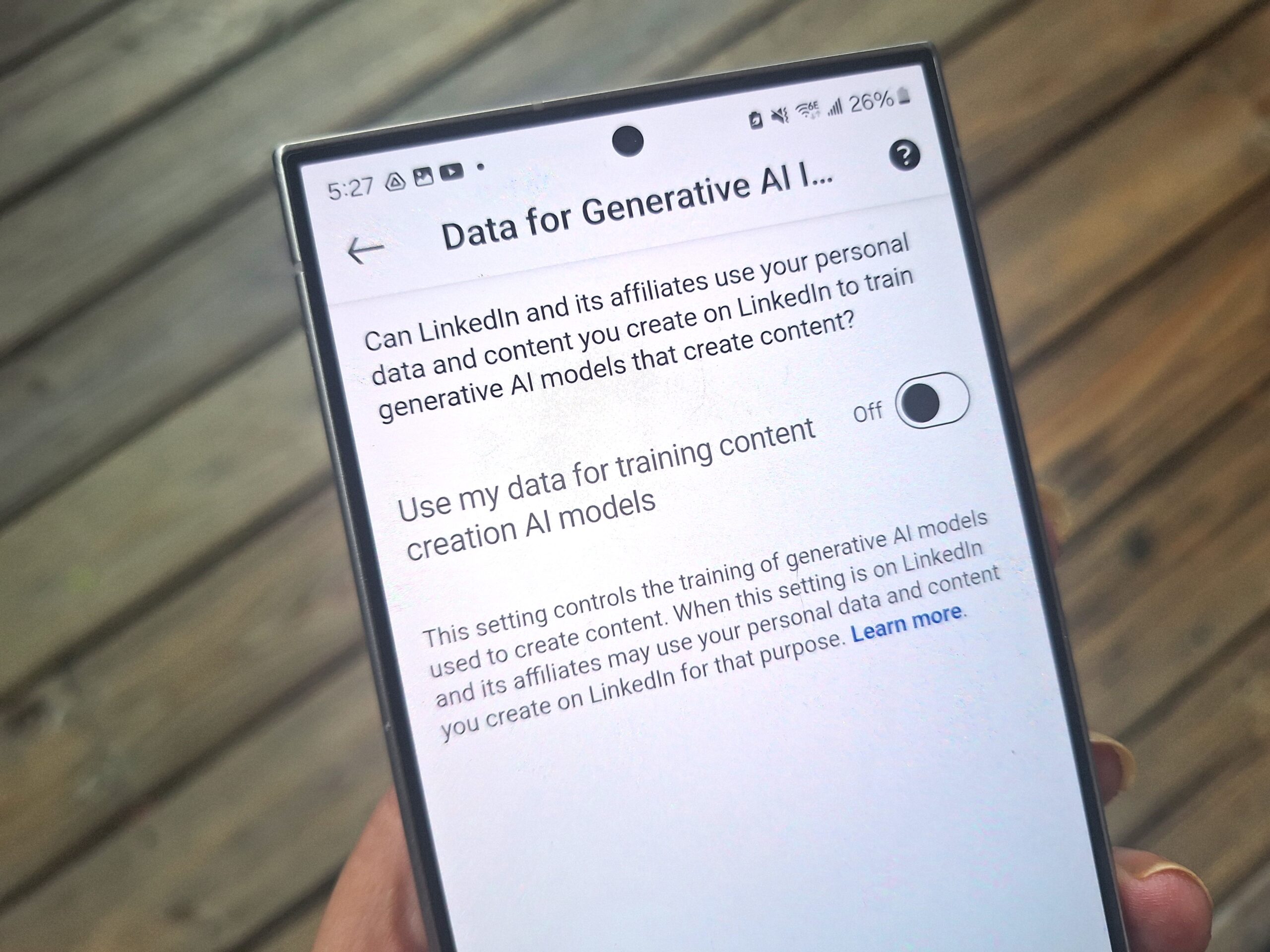 A smartphone screen displays a LinkedIn setting to enable or disable the use of personal data for training generative AI models.