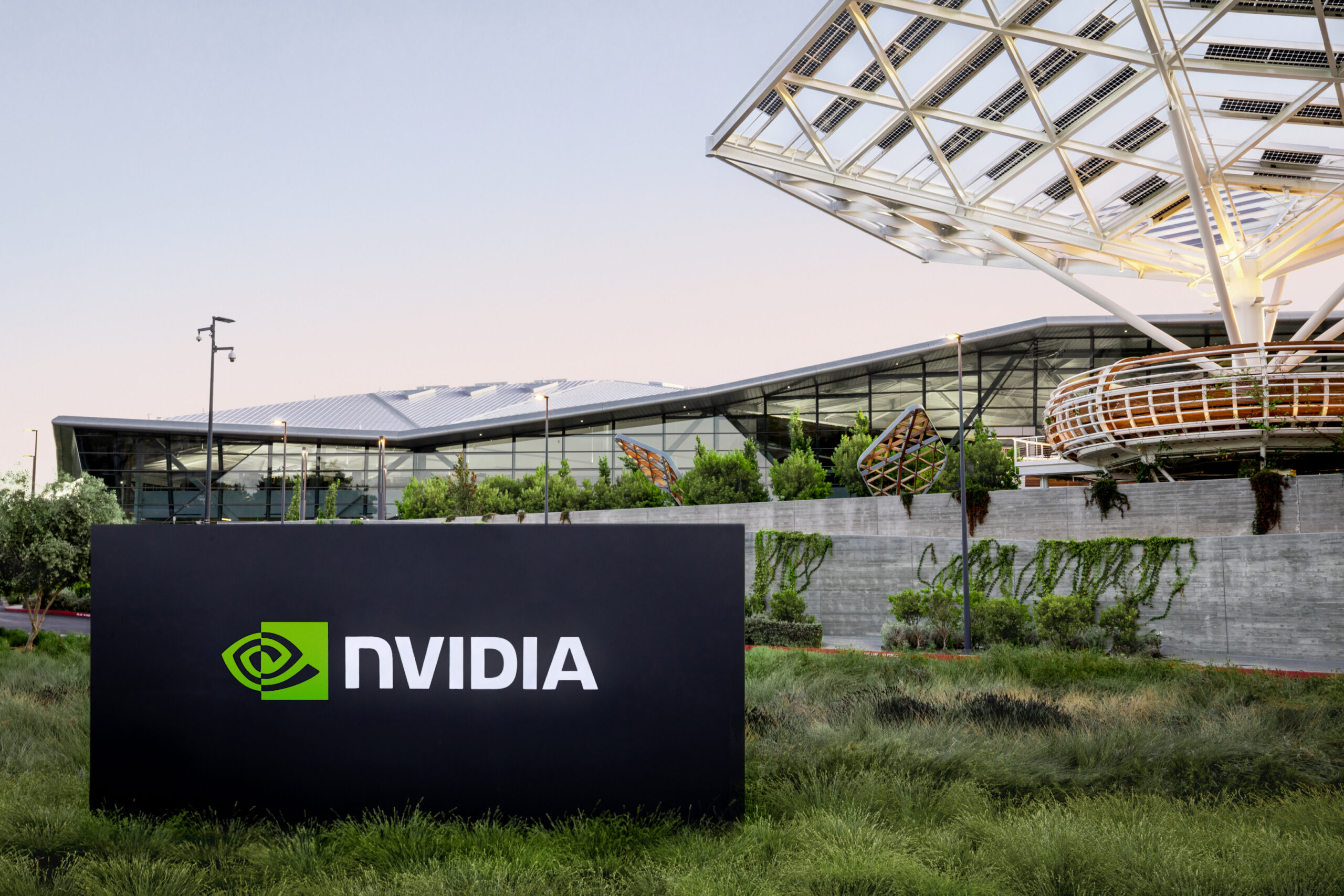 NVIDIA sign in front of a modern building with a geometric roof structure and landscaped surroundings.