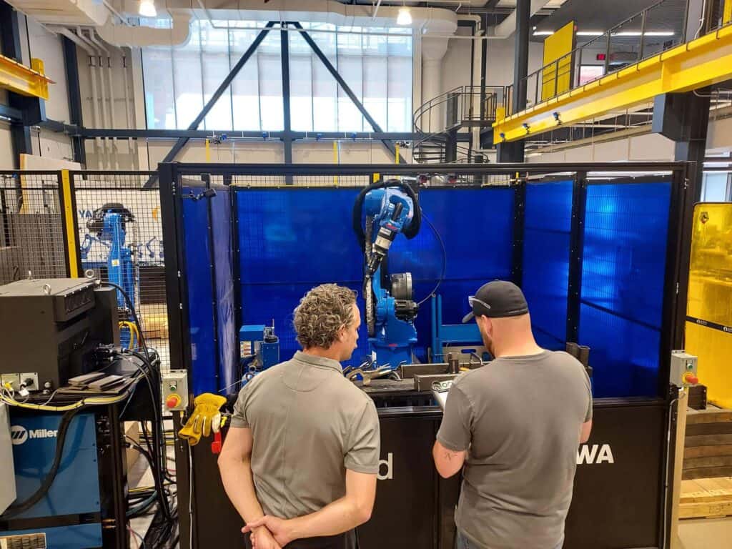 Two man stand in front of a robot at the ARM Institute.