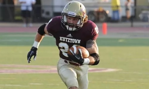 A football player in a maroon jersey and gold helmet runs with the ball on a field.