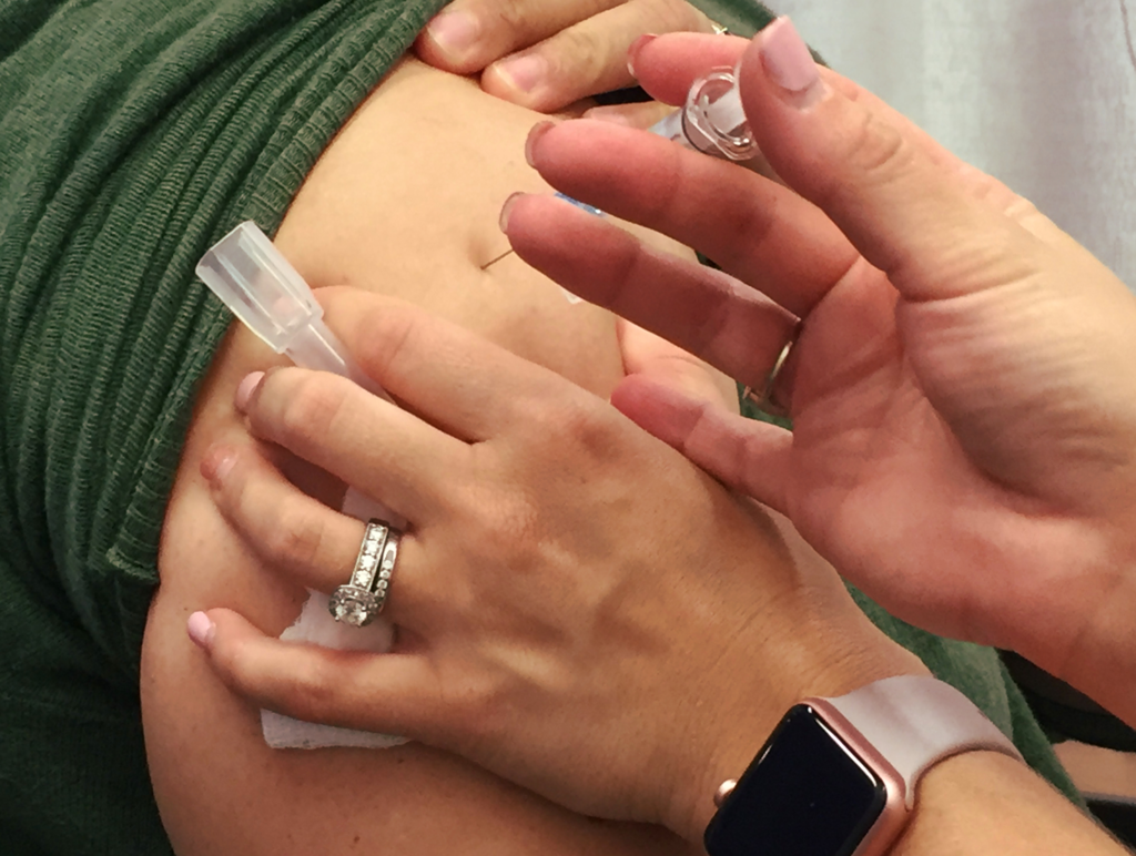 A person receives a vaccination in their upper arm, with a healthcare professional holding the needle and vial.
