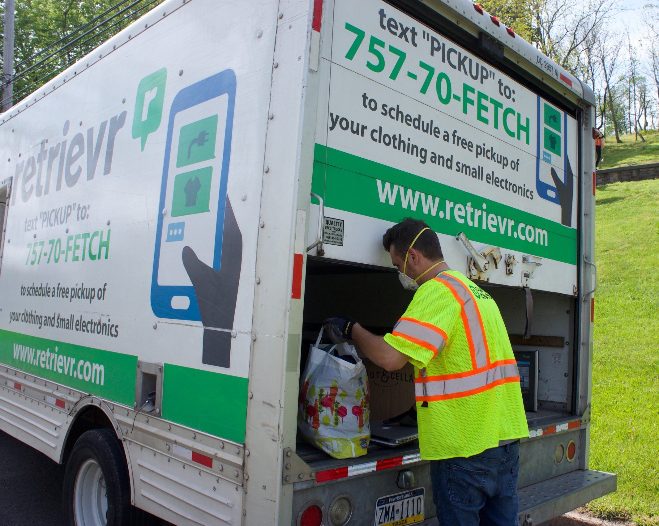 A person in a high-visibility vest organizes collected items in the back of a recycling truck labeled "retrievr" for clothing and small electronics pickup.