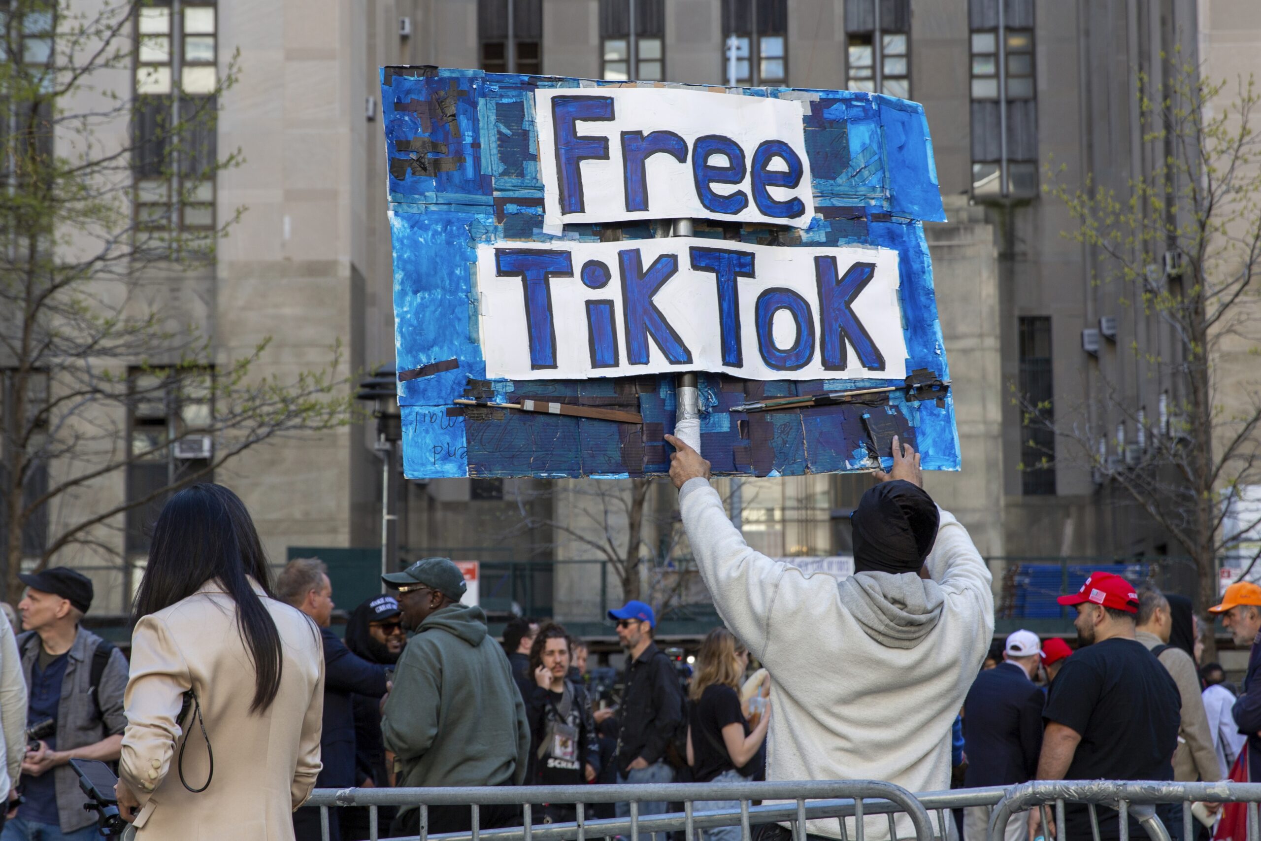 Person holds a "Free TikTok" sign at a public demonstration in an urban setting.
