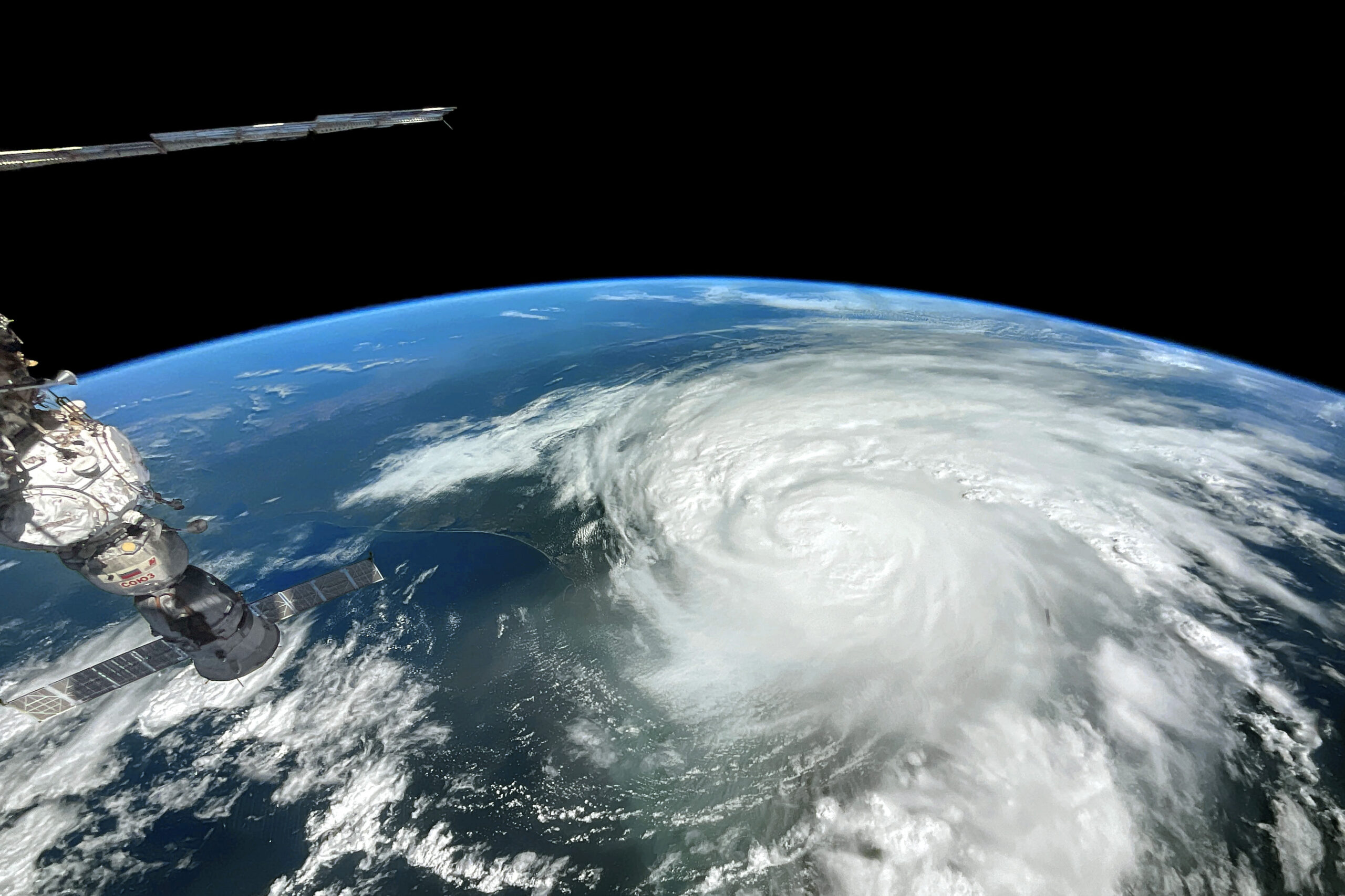 Part of a spacecraft sticks out over a blue Earth with a massive white hurricane in the center