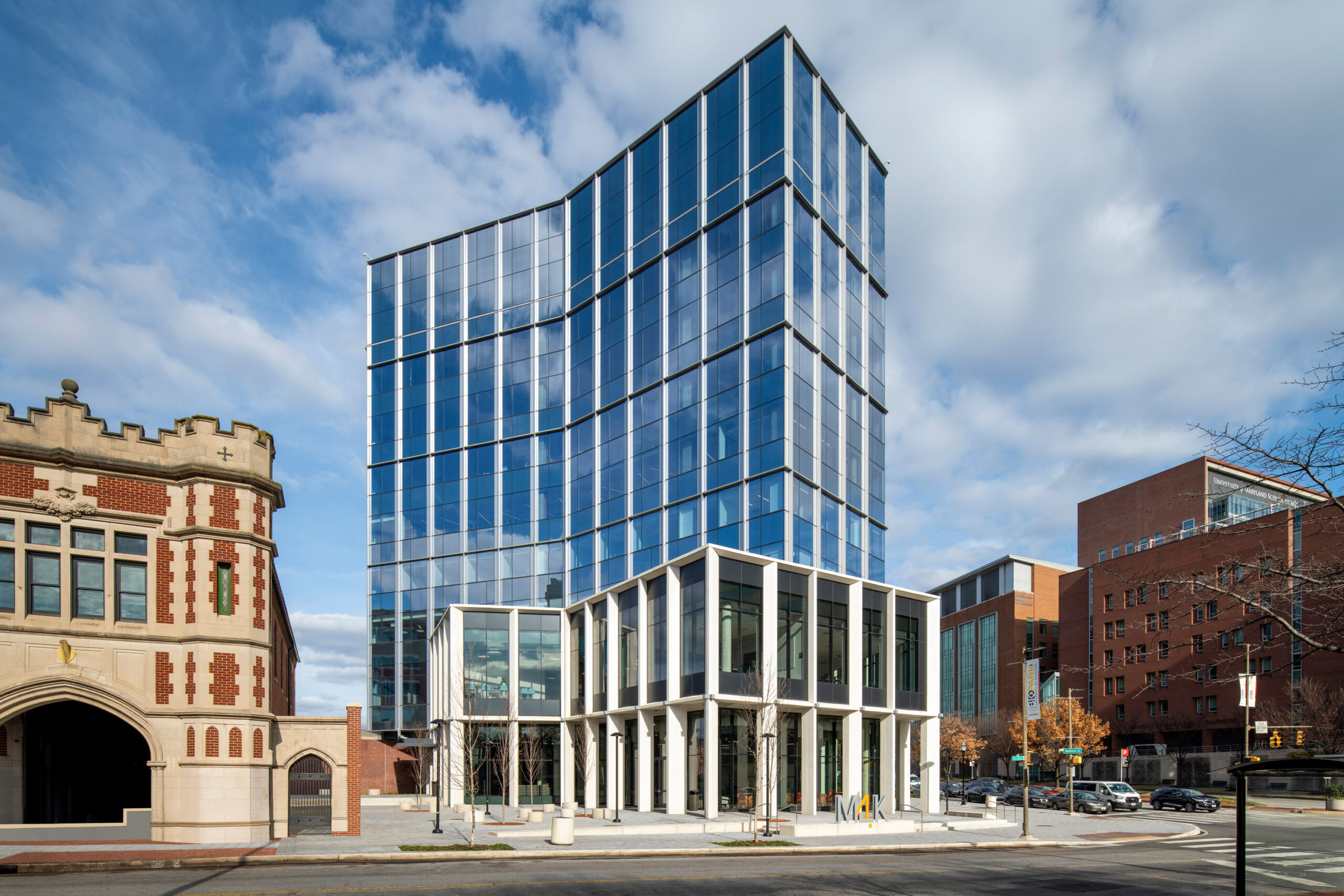 A glass building with white and grey architecture stands in front of a blue sky, near red brick buildings