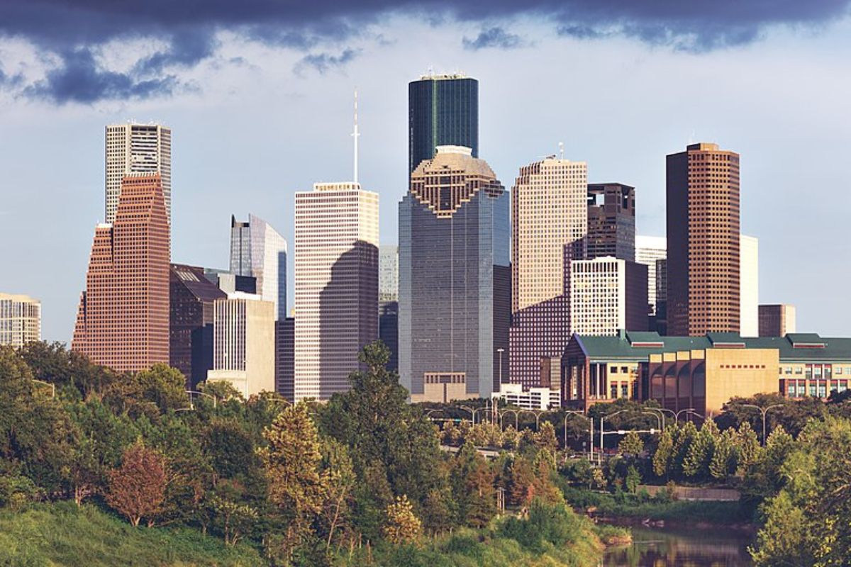 Skyline of downtown Houston with various skyscrapers, trees, and a cloudy sky.