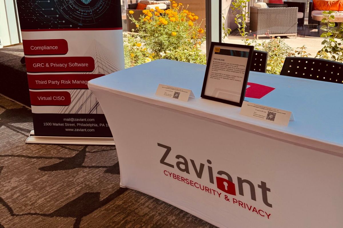 An exhibition table with a Zaviant Cybersecurity & Privacy banner, informational display, and materials. Background shows flowers and patio seating.
