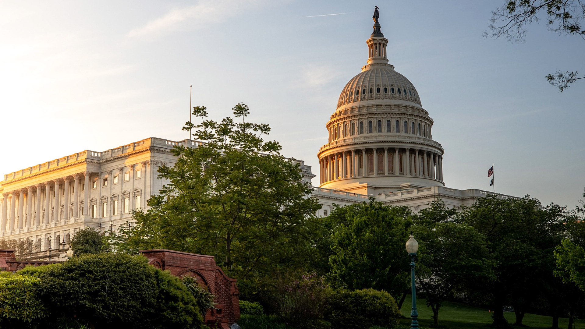 The U.S. Capitol building with a dome and columns, surrounded by trees, under a clear sky at sunset.