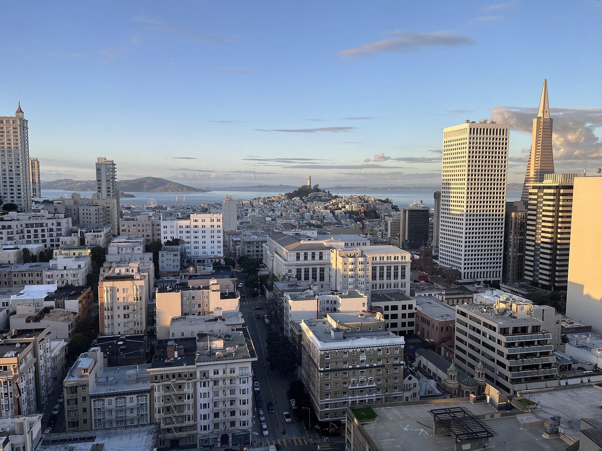A cityscape view of San Francisco featuring a variety of buildings, with Coit Tower in the distance and water visible on the horizon.