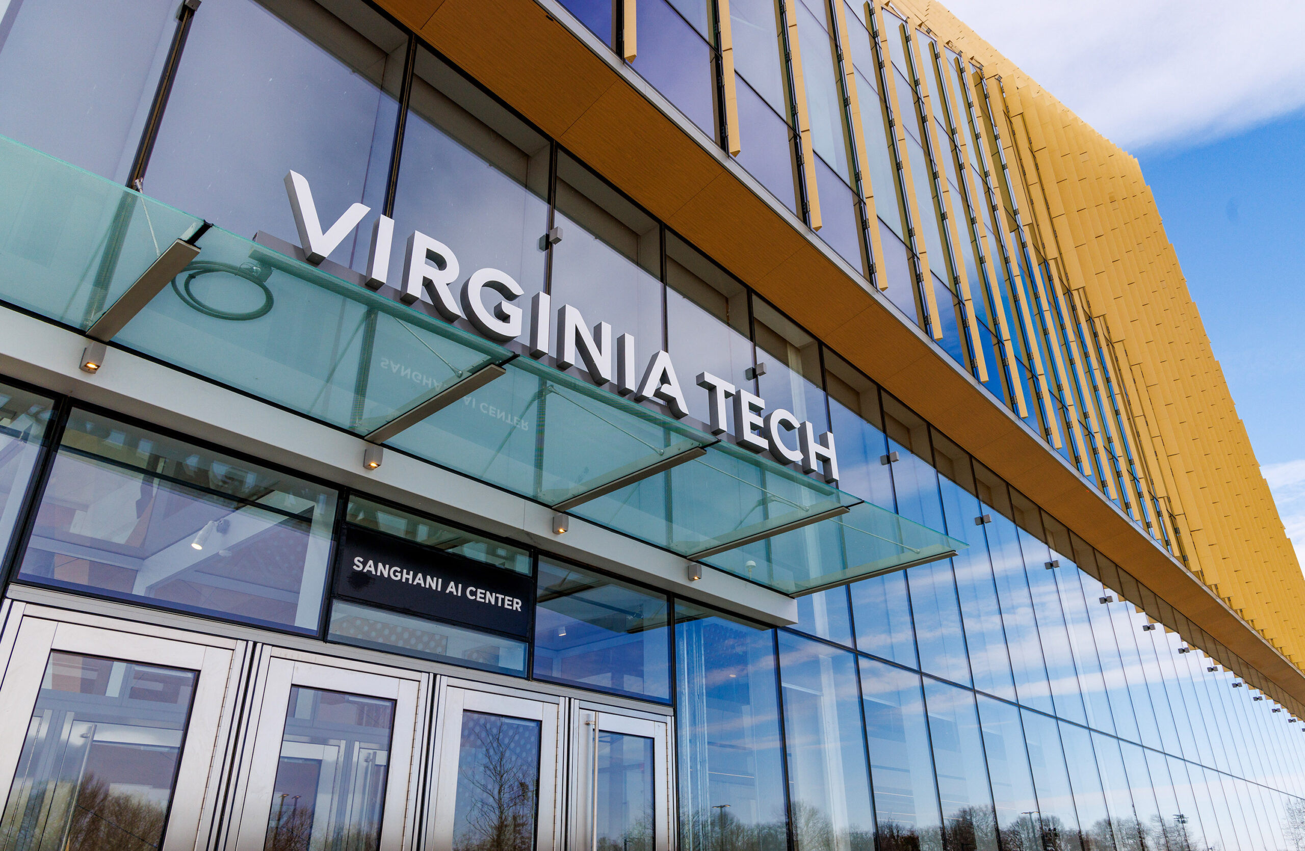 Exterior view of the Virginia Tech Sanghani AI Center, featuring large glass windows and the building's name prominently displayed above the entrance.